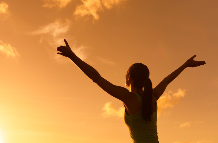 Happy woman with arms up in the sunset.