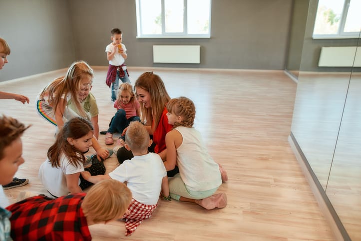 Spending time with kids. Full length portrait of positive dance teacher talking to group of little girls and boys sitting on the floor in studio Full length portrait of positive dance teacher talking to group of little girls and boys sitting on the floor in studio. Relationship between teacher and kids. Choreography class. Dance school