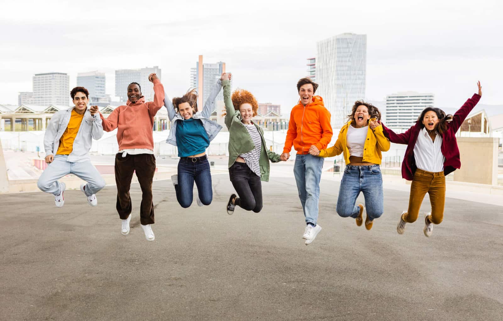 Diverse happy group of young friends jumping together outdoors Diverse happy group of young friends celebrating having fun outdoors. Community concept with teenage people jumping holding hands over city urban background
