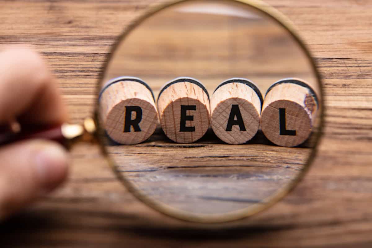 Hand Holding Magnifying Glass In Front Of Real Text Close-up Of A Person Examining Real Corks Through Magnifying Glass On Wooden Table