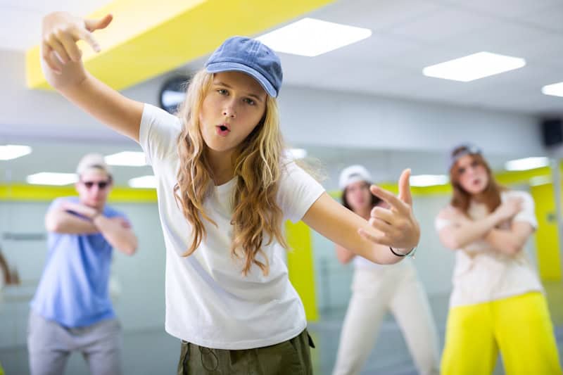 Cool talented teens in casual wear exercising modern dance moves in training room Expressive cool young dancers rehearsing their new dance during training together in studio