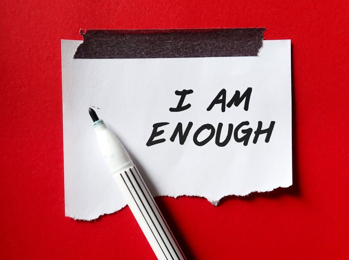 Stick note on red background with pen writing text I AM ENOUGH, Positive mantra affirmation to boost self acceptance, Knowing that you are worthy, valid, acceptable, loved. Embrace all flaws and imperfection I am enough
